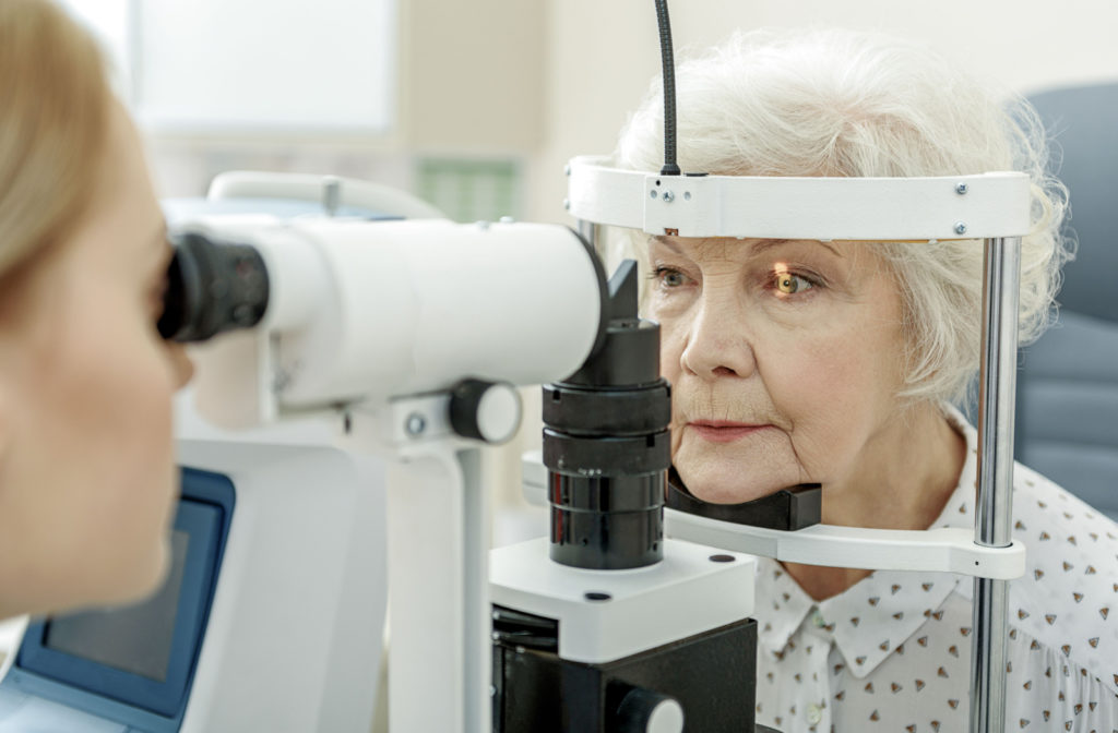 An optometrist performing a slit-lamp exam on an older adult woman.