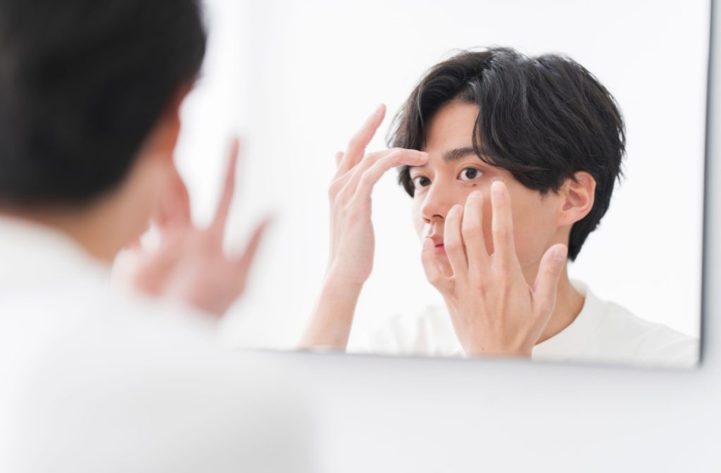 A man wearing contact lenses in front of a mirror.
