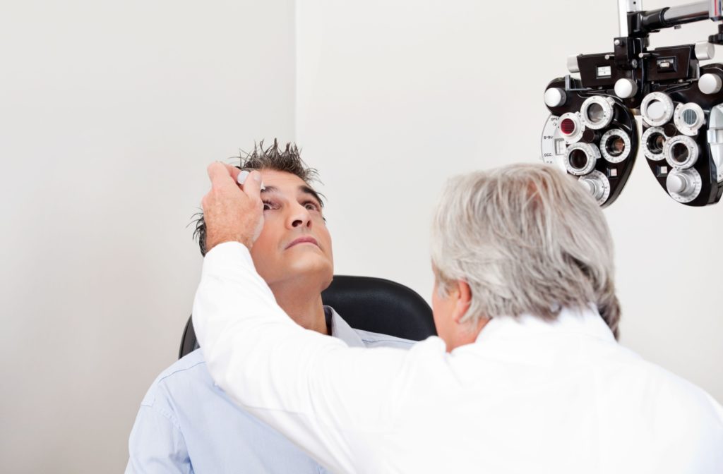 An optometrist applying eye drops to the right eye of his patient to alleviate eye dryness.