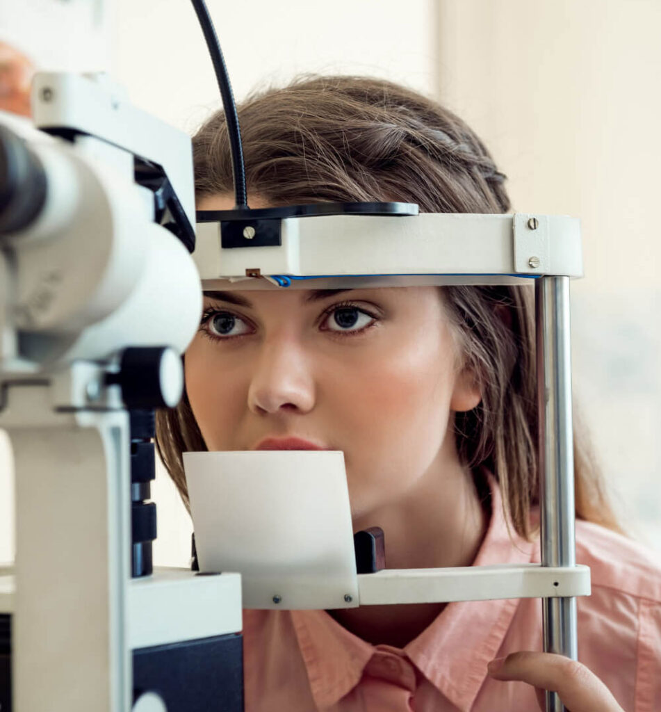 Patient rests their chin on an eye exam machine during a vision test in a clinical setting. The image represents comprehensive eye exams in Toronto that support clear vision and long term eye health.